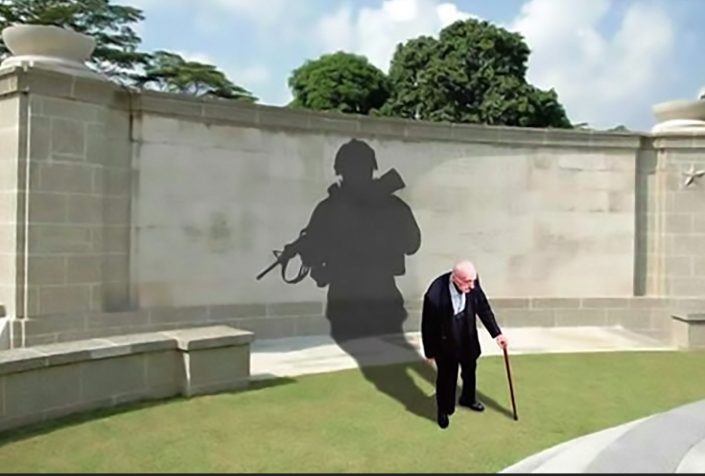 Elderly veteran standing before the shadow of his younger military service