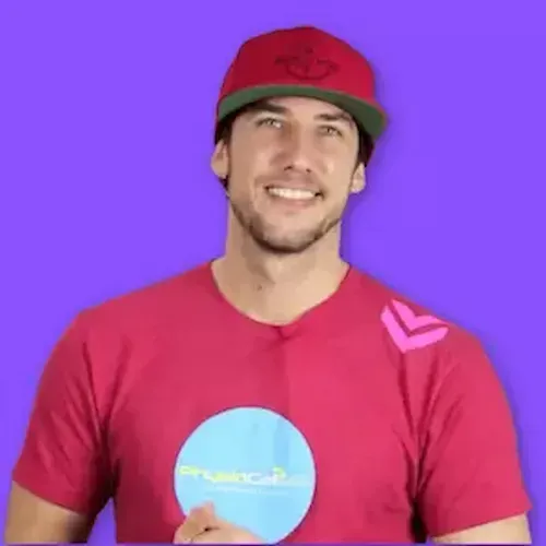  A smiling man with dark wavy hair and a thick mustache, wearing a bright blue Asics sports shirt, standing in front of a solid yellow background.