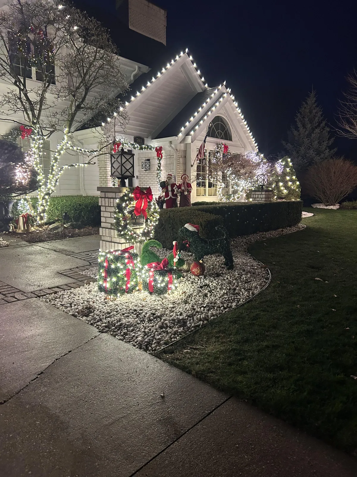 House at dusk decorated with white holiday lights outlining the roofline and garage, plus wreaths and lit garlands.