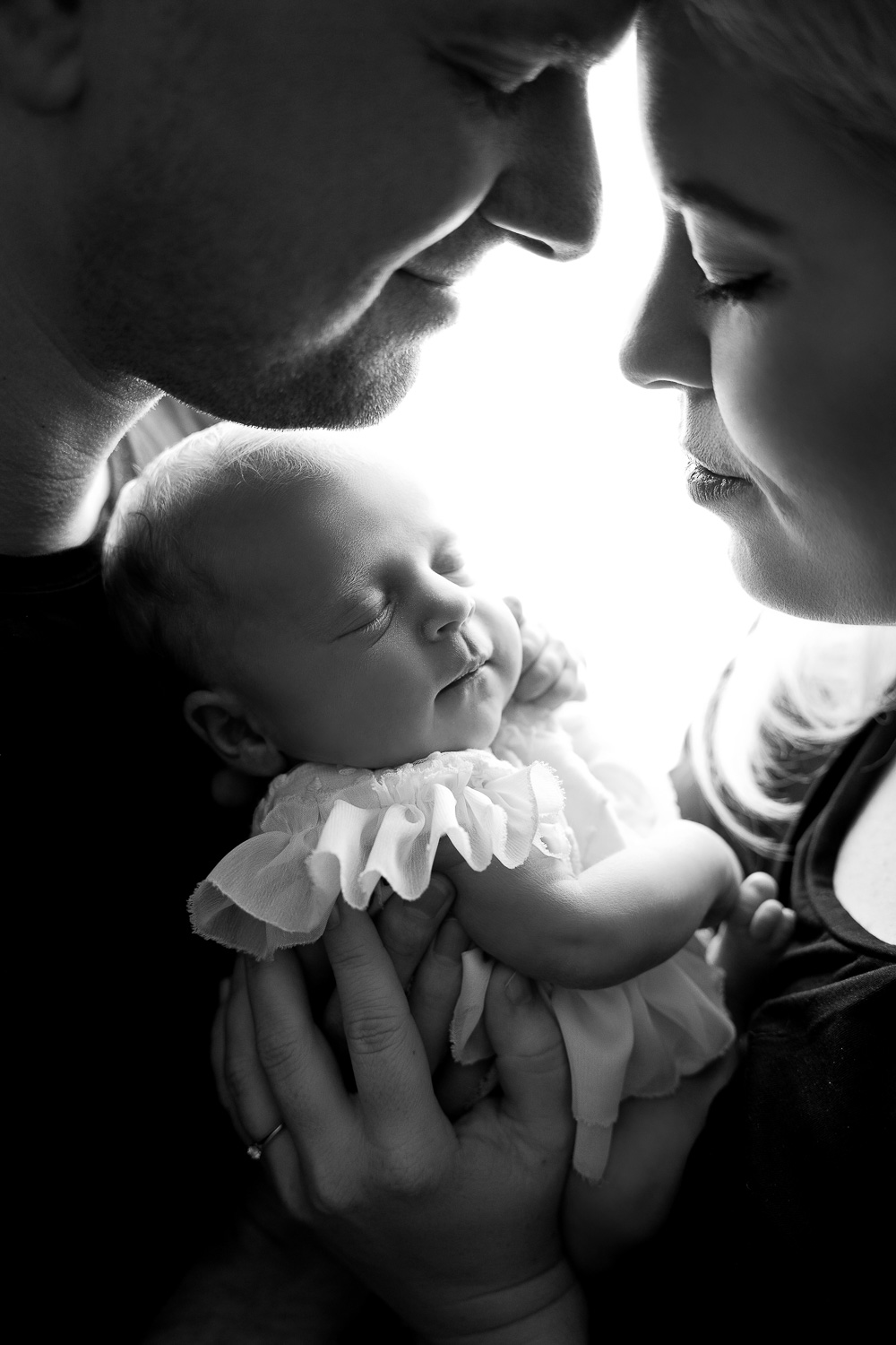 Familienbild mit Baby im Gegenlicht beim Shooting Hamburg, links und rechts sind Papa und Mama und in der Mitte das Baby, zeitlos und in schwarz weiß