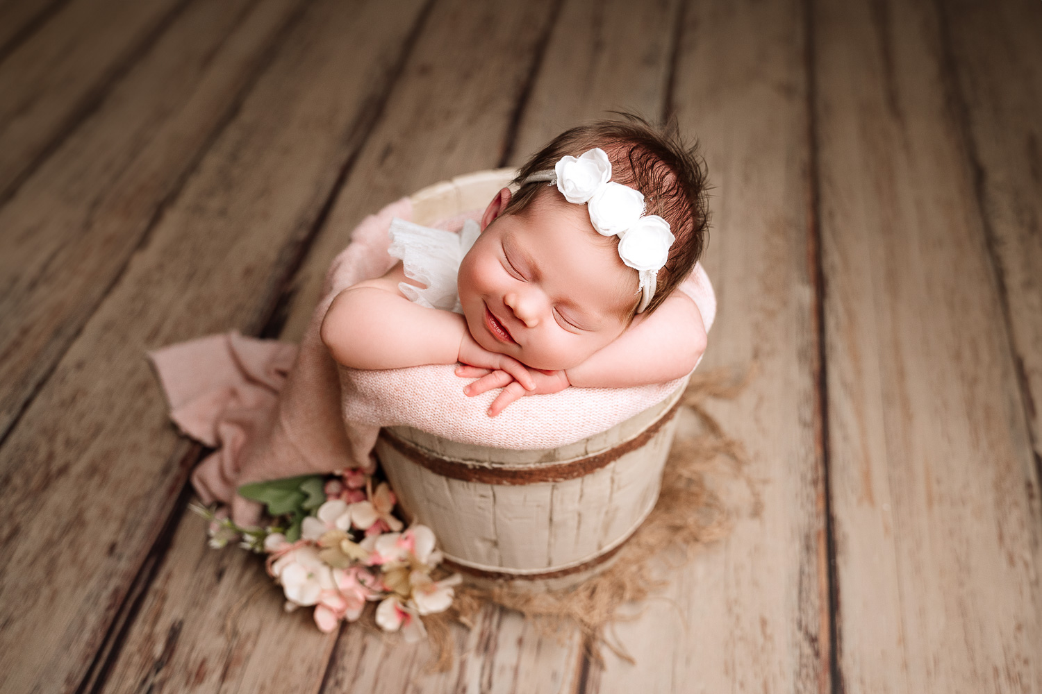 Babymädchen beim Neugeborenen-Shooting in einem rustikalen Eimer positioniert in rosa und brauntönen