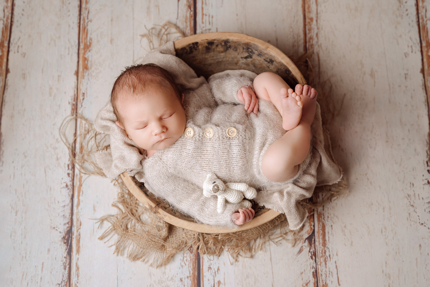 Babyjunge in einer rustikalen braunen Schale in einem Strickoutfit, Teddybär im arm schlafend