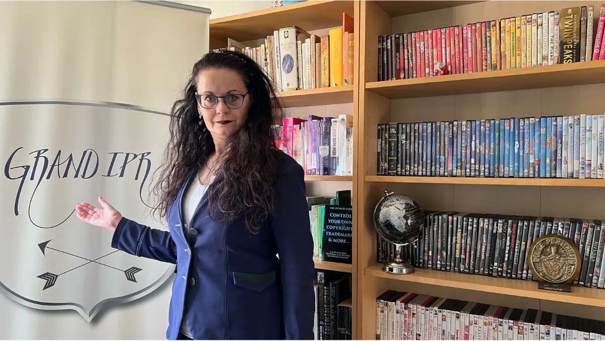 Image of Céleste between her colour coded book / DVD ase and banner with hand twoard banner palm up