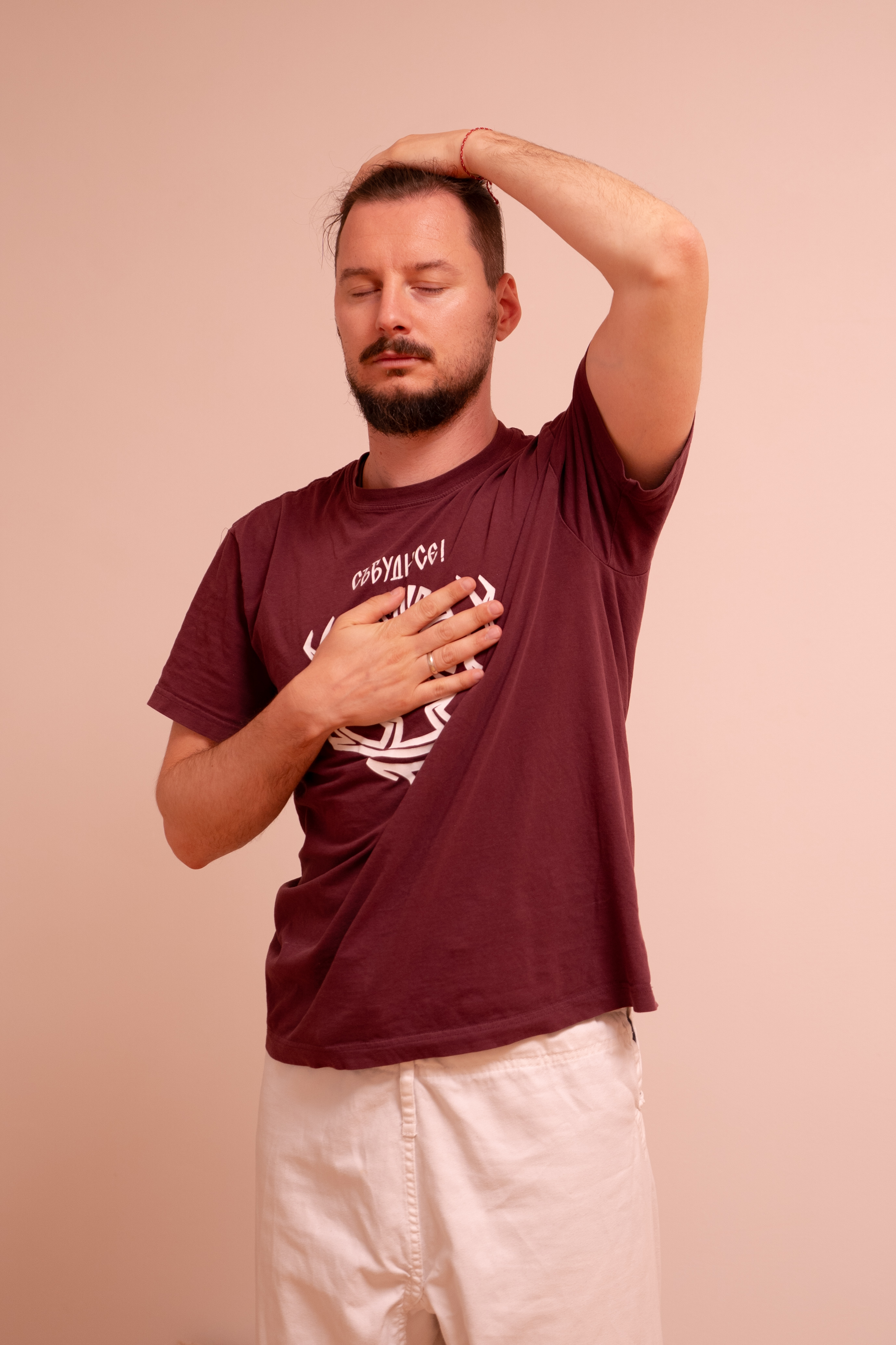 Спокойна жена в края на 30-те, облечена в свободни естествени дрехи, седнала със скръстени крака на постелка, с затворени очи и внимателно поставени ръце на гърдите, в залята от слънце студио с нежни зелени растения и дървен под, излъчваща спокойствие и връзка със себе си.