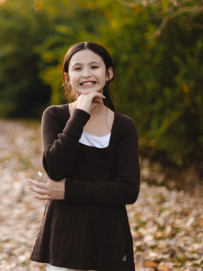 Young girl smiling on a leaf covered path during a fall children's portrait session with Andria May Photography in Gilbert, AZ