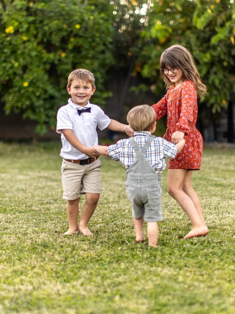 Three siblings holding hands and playing together outdoors during a family photography session with Andria May Photography in Gilbert, AZ