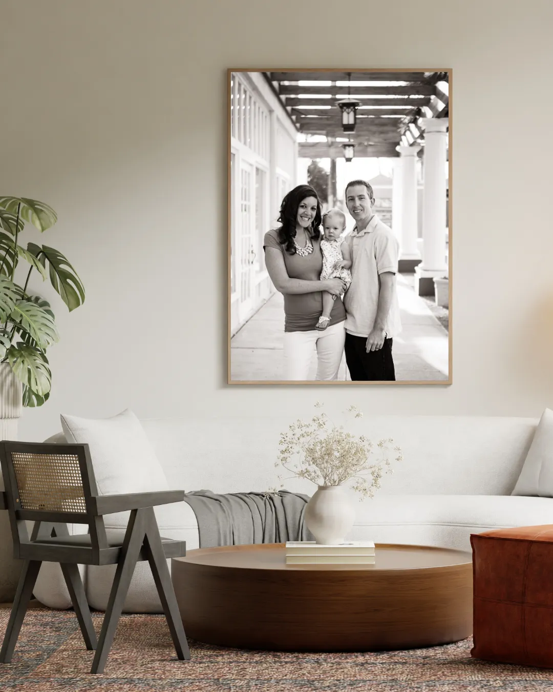 Black and white family portrait of a mom, dad and toddler, framed as wall art above a sofa in a living room