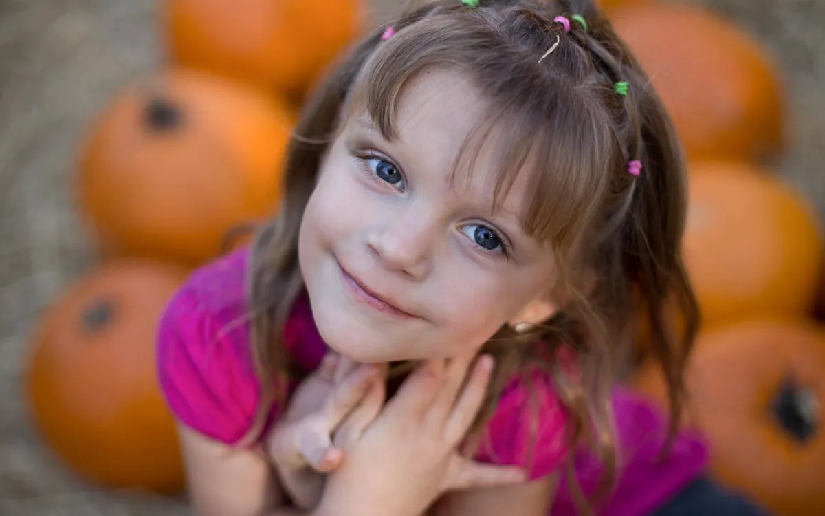 Young girl smiling with her chin resting on her hands at a pumpkin patch during a fall children's portrait session with Andria May Photography in Gilbert, Arizona