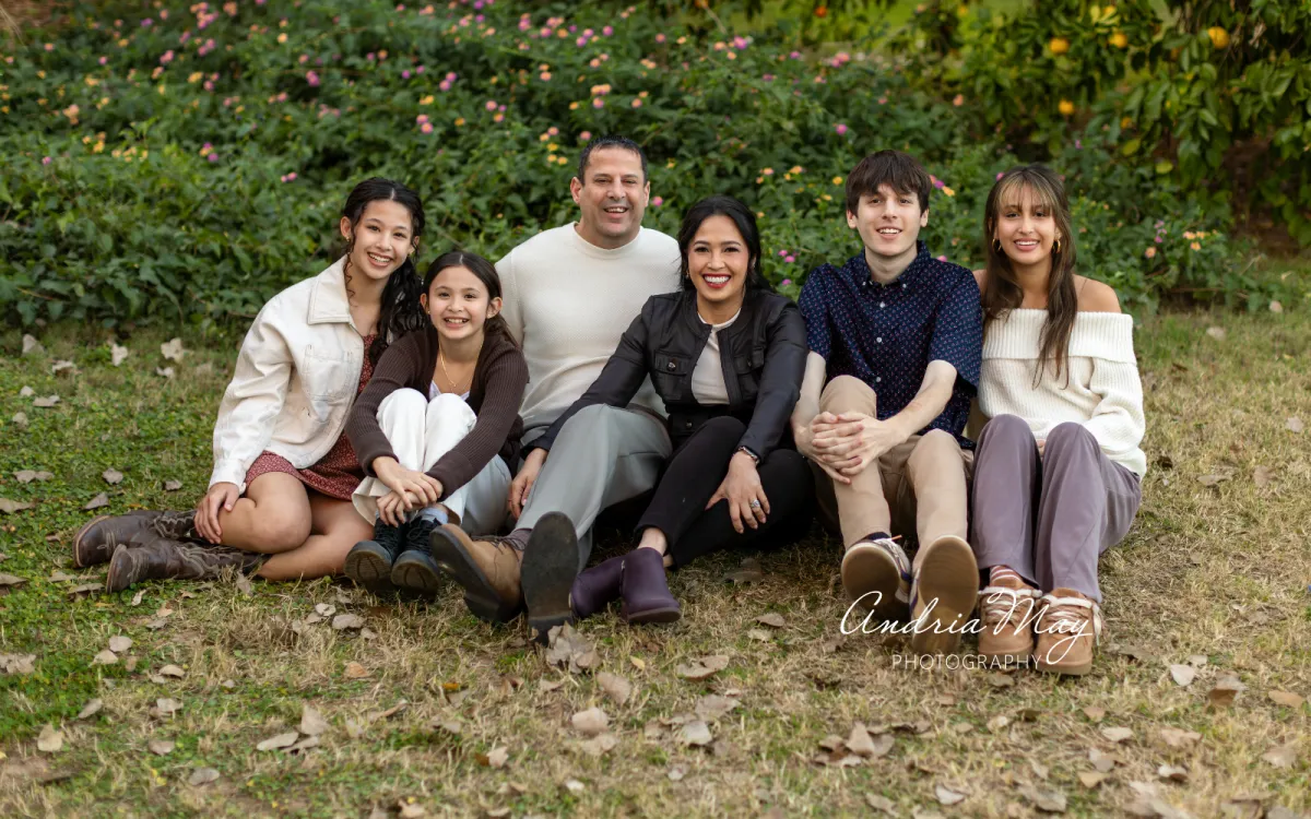 Family of six sitting together outdoors on fallen leaves, captured by Andria May Photography, a family photographer in Gilbert, Arizona