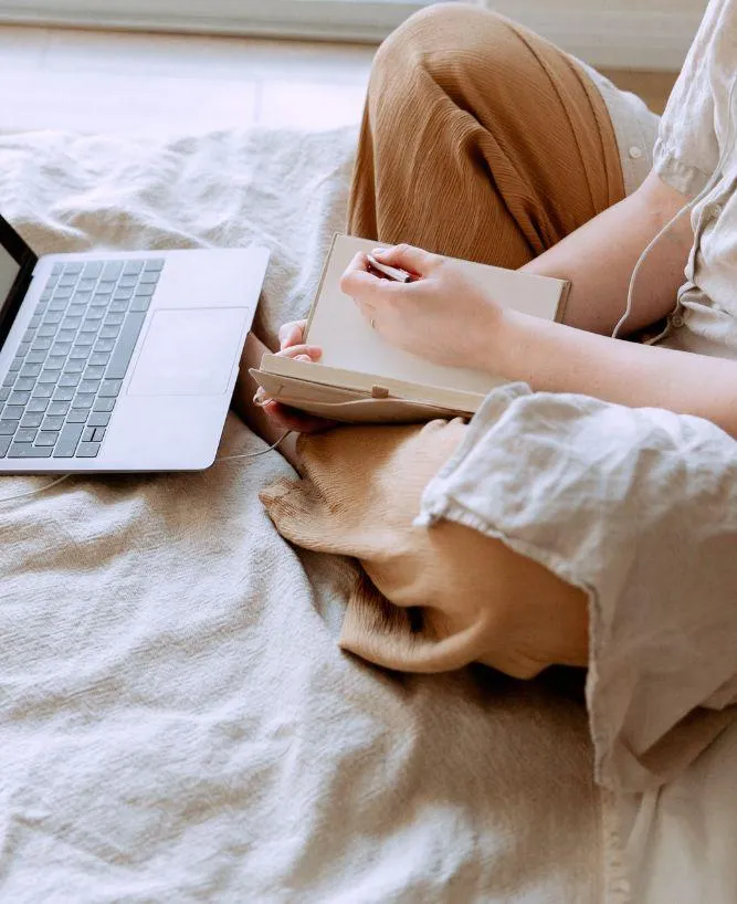 Woman sitting cross-legged with laptop and notebook, representing business owners overwhelmed by tech tasks and seeking streamlined solutions.