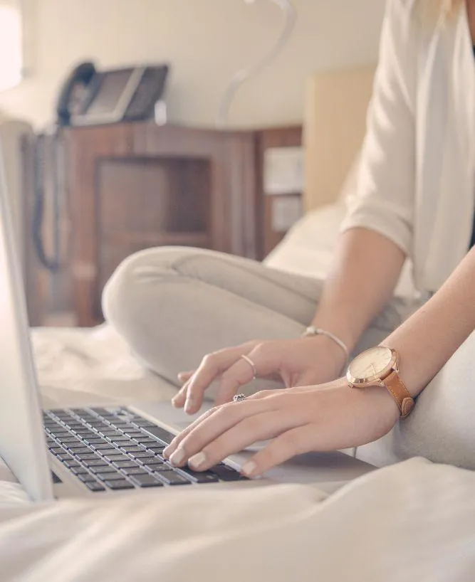 Stock photo of a woman's hands on a laptop sitting on a bed, symbolizing a relaxed approach to starting a strategy session to simplify business tech.