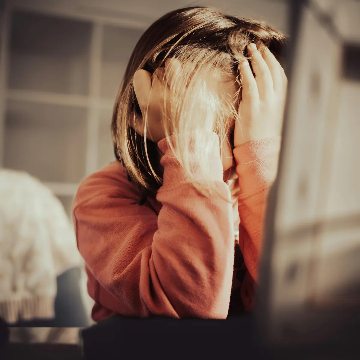 young girl with face covered by hands in front of a computer screen
