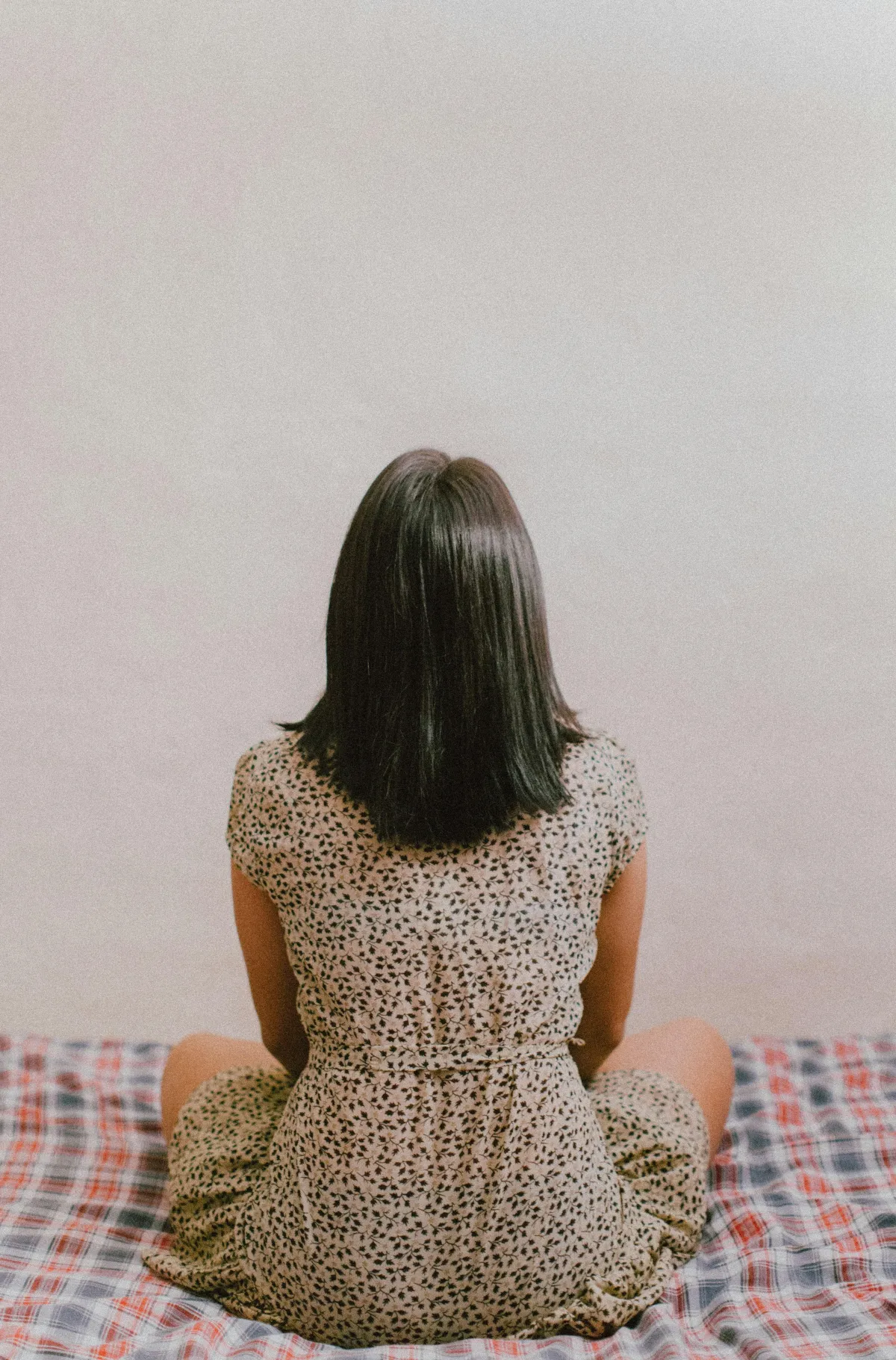 female sitting on a bed, back turned, staring at the wall