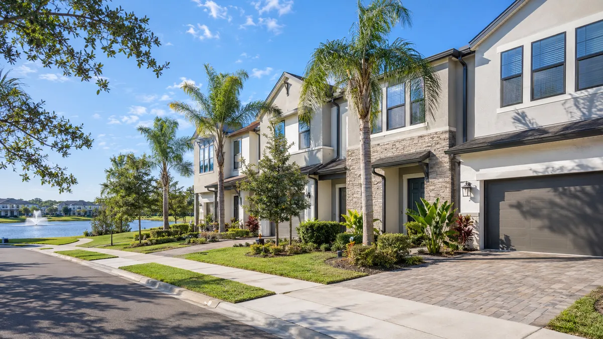 Modern Lake Nona townhomes in Orlando, Florida, with palm trees, landscaped sidewalks, attached garages, and a lake with fountain, representing the Lake Nona townhome real estate market in July 2026.