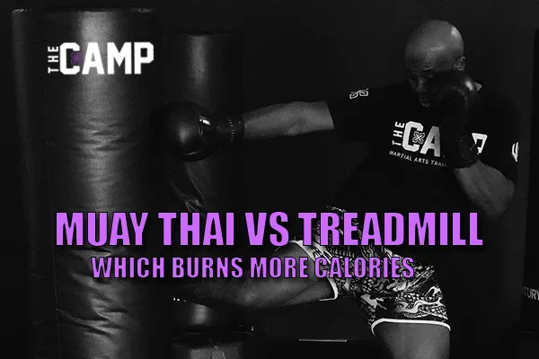 Coach executing a powerful low roundhouse kick on a heavy bag during Muay Thai conditioning at The Camp MATC