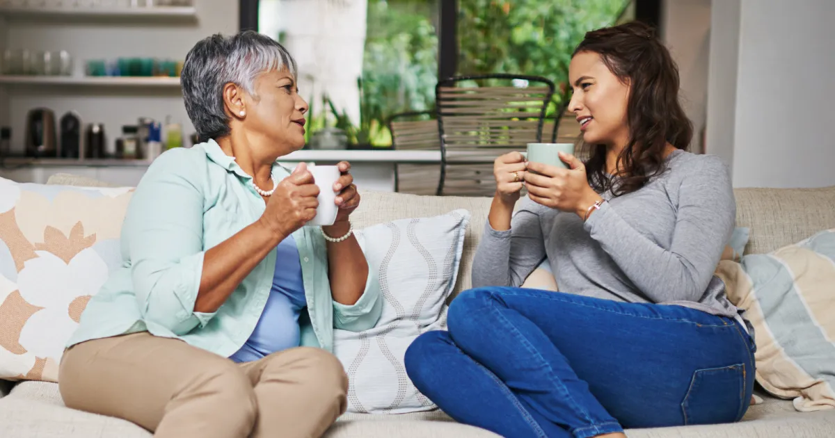 Elder mother and adult daughter talking with a cup of coffee in hand