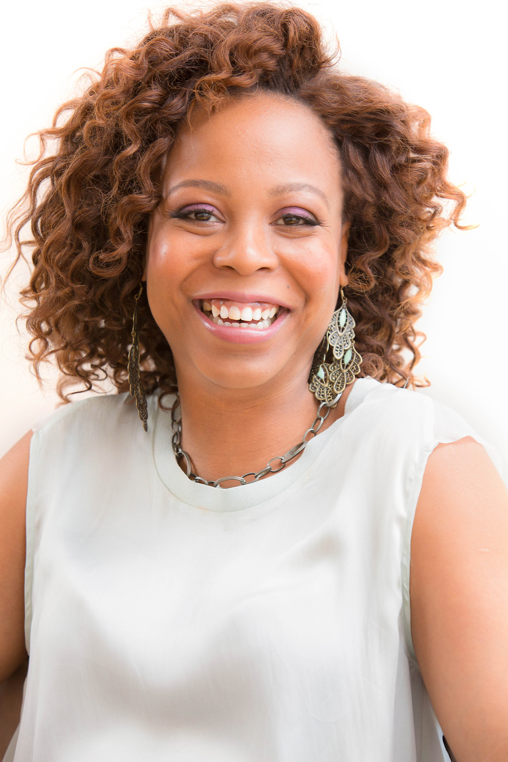 An African American woman with wide smiles and short brown curly hair wearing an ash coloured top