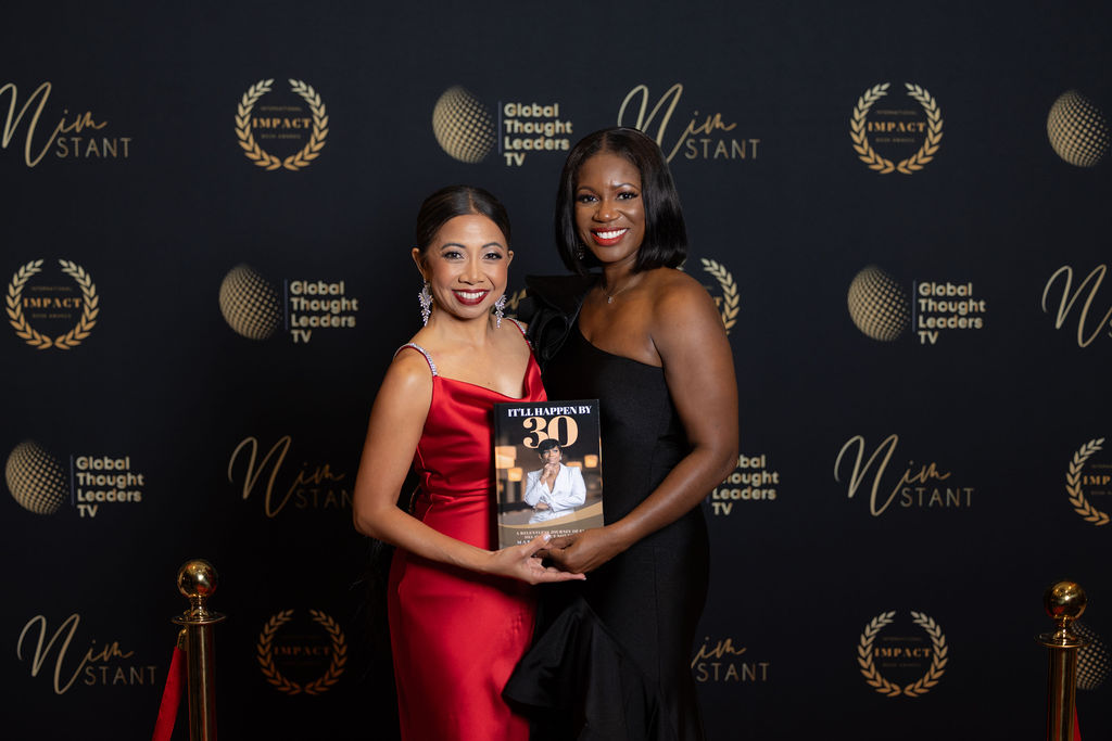 Two authors holding an award-winning book on the press wall at an IIBA event.