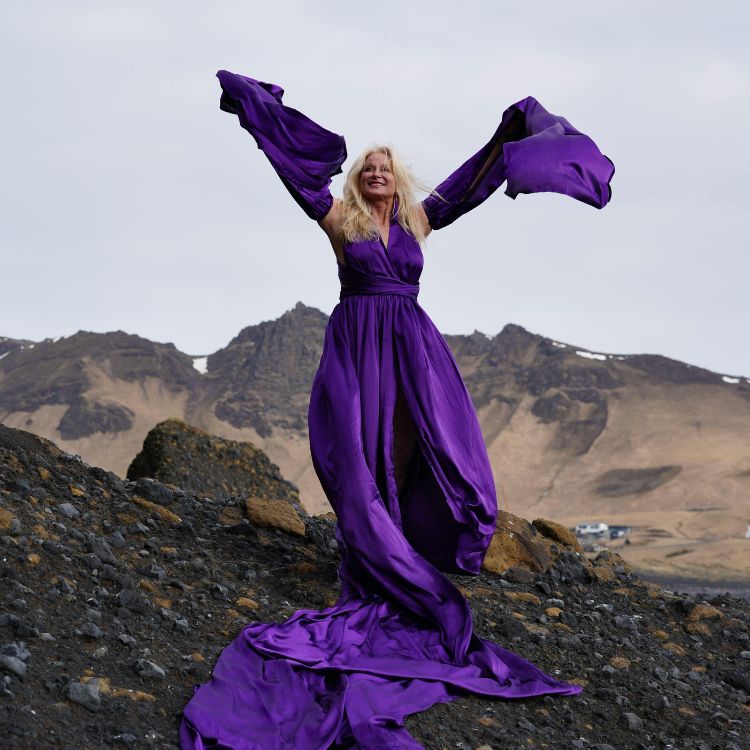 woman in a long purple dress wiht her arms in teh ir
