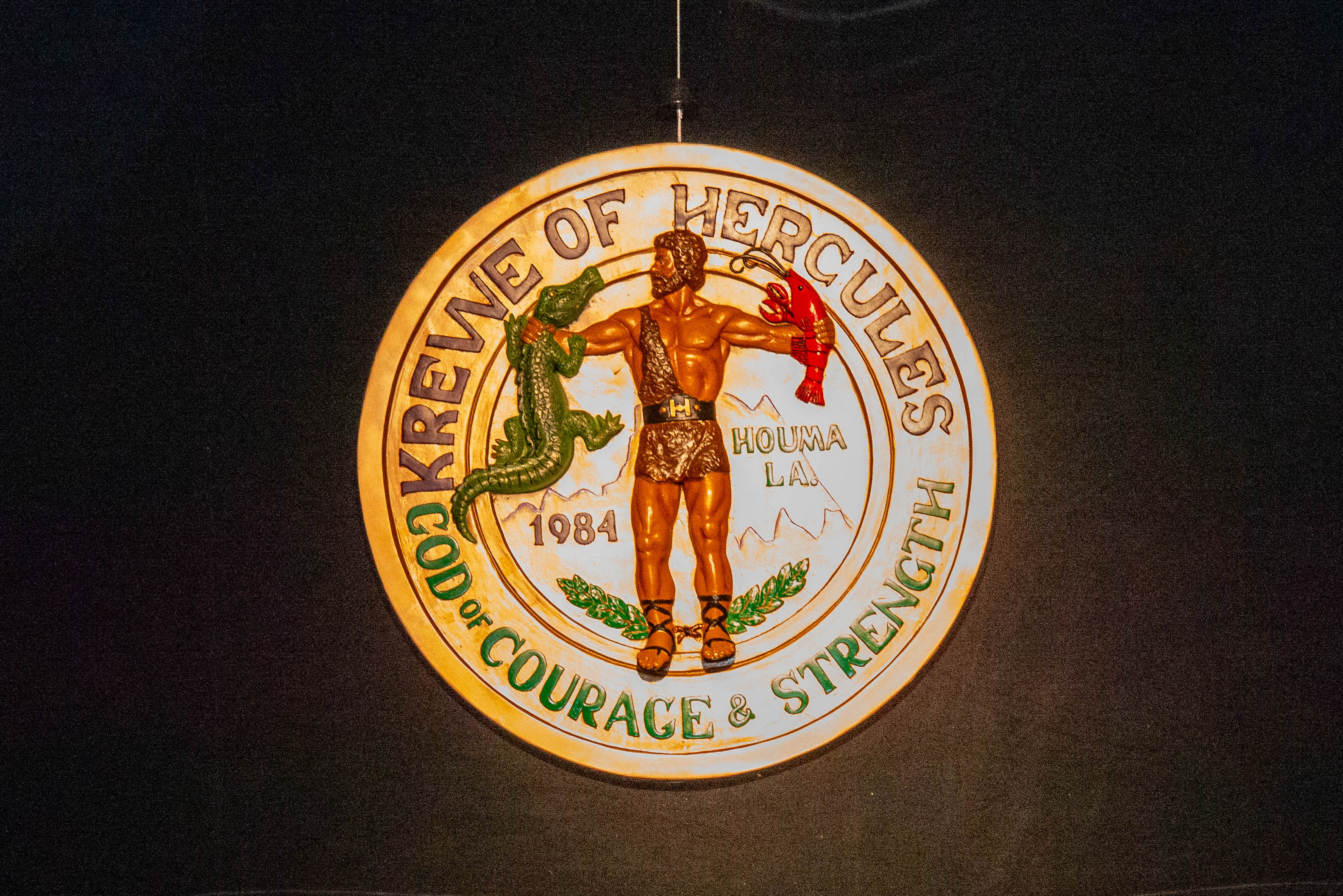 A vibrant, detailed 3:2 image of a Hercules Krewe parade float, adorned with gold, purple, and green decorations, rolling through a lively Mardi Gras street with costumed members waving to a cheering crowd. The background features festive banners and confetti, capturing the excitement and energy unique to the Krewe's parade experience.