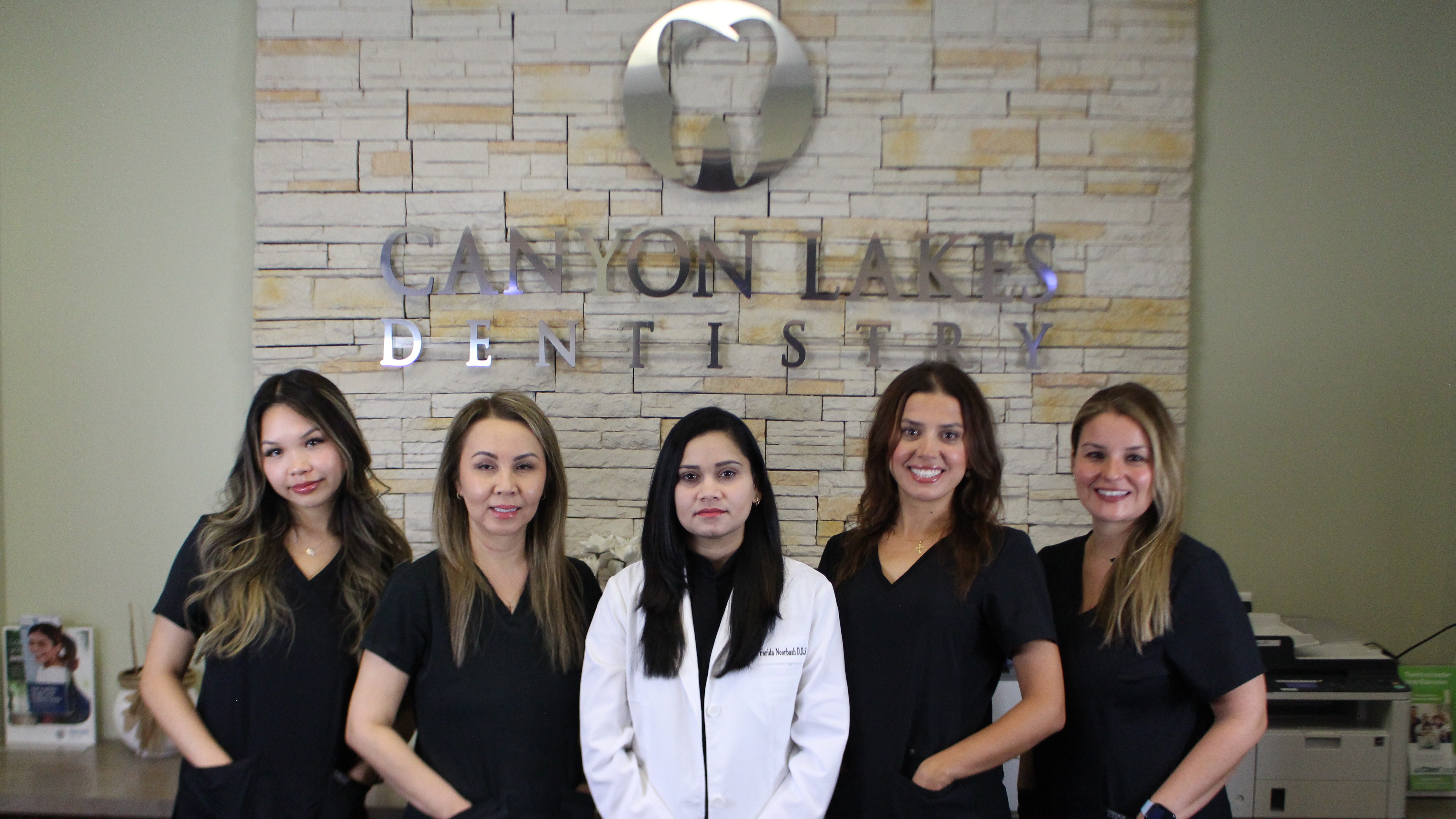 Photo of team members from Canyon Lakes Dentistry in front of the logo in their office