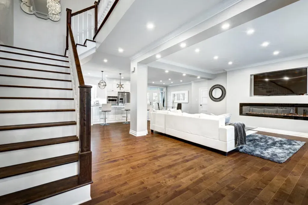 "Bright and luxurious open-concept living room and kitchen renovation by B&Y Reno Corp, featuring hardwood flooring, recessed lighting, a floating fireplace, and modern staircase design."