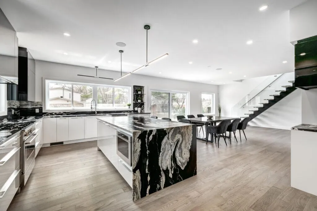 Modern open-concept kitchen and dining area with black and white marble island, sleek cabinetry, and floating glass staircase — B&Y Reno Corp project