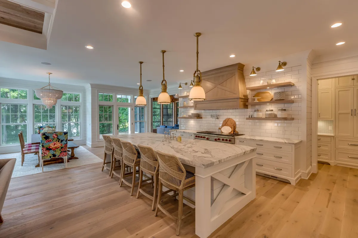 Bright farmhouse-style kitchen featuring a large marble island, rattan bar stools, pendant lighting, and custom cabinetry — completed by B&Y Reno Corp.