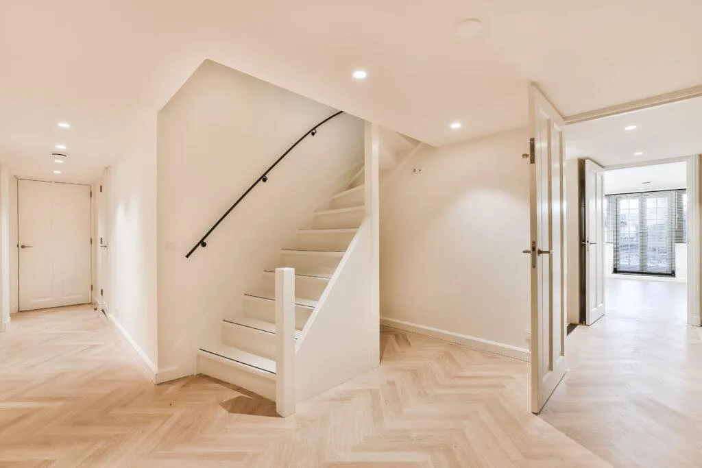 "Modern legal basement renovation with herringbone flooring, white staircase, and recessed lighting — expertly finished by B&Y Reno Corp."