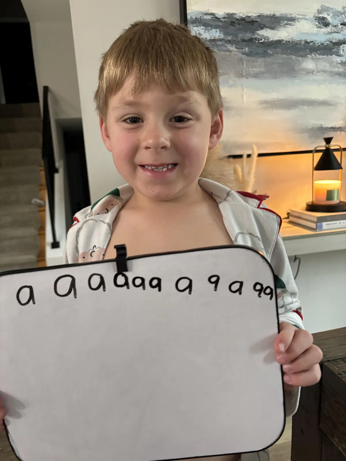 A smiling young child, around six years old, sits at a kitchen table with a colorful workbook open, tracing letters with a bright yellow pencil. Sunlight streams in from a window, and a parent gently encourages from the side. The scene is warm, inviting, and filled with hope.