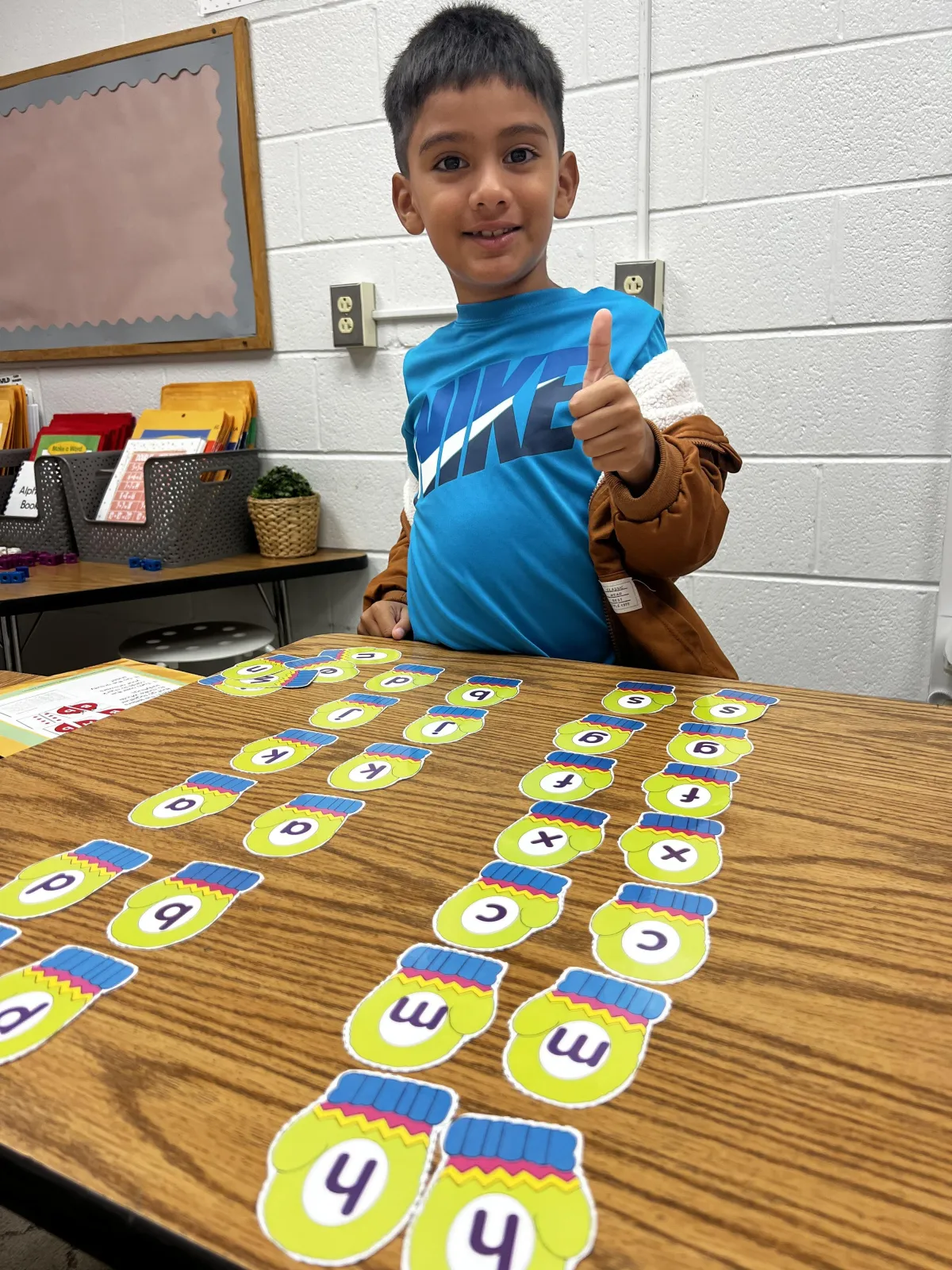 A diverse group of children, ages five to seven, gather around a table with colorful letter tiles and flashcards. An enthusiastic teacher demonstrates a phonics game, while the children laugh and participate. The classroom is bright, with educational posters and cheerful decor.
