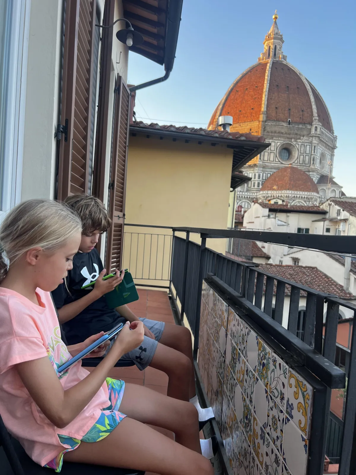 A young boy, age seven, beams with pride as he holds up a completed reading worksheet. His mother, smiling, gives a thumbs up in the background. The room is filled with books and educational posters, creating a positive, achievement-focused atmosphere.