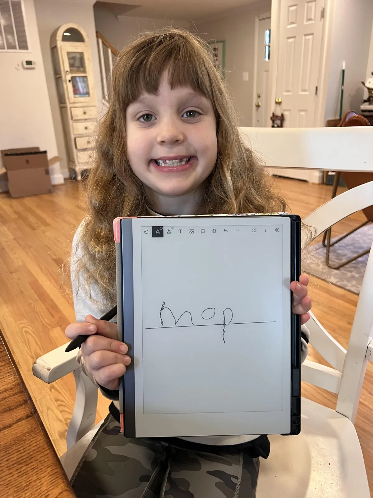 A worried parent, mid-30s, sits beside a frustrated child at a dining table covered with reading worksheets. The child, a first grader, looks down, pencil in hand, while the parent gently rests a hand on their shoulder. The background is a cozy, lived-in home.