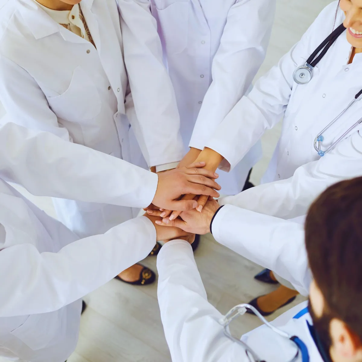 A group of healthcare professionals standing in a circle, with their hands clasped together in unity.