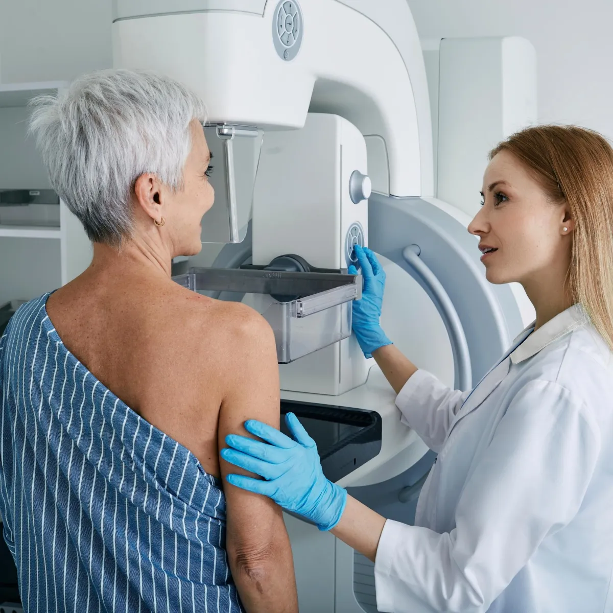 A healthcare professional is assisting a patient in performing a mammogram.