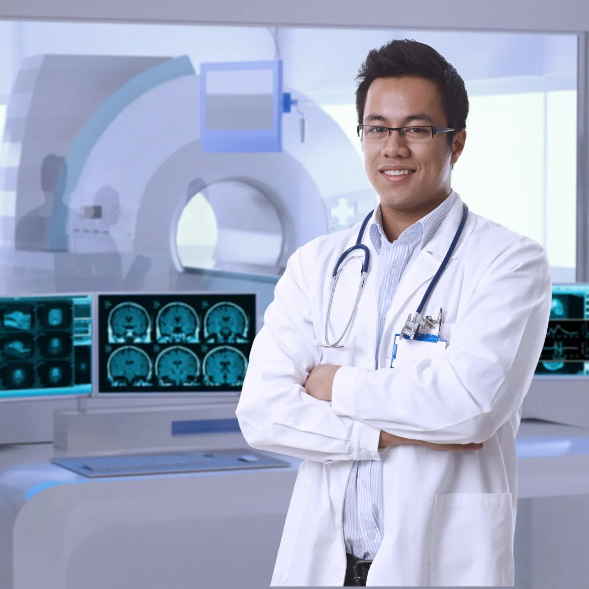 A doctor, standing with arms crossed, standing in front of a computer screen displaying medical images.