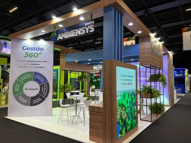 A well-lit corporate exhibition booth featuring a large 'Gestão 360°' display, tables, and green chairs.