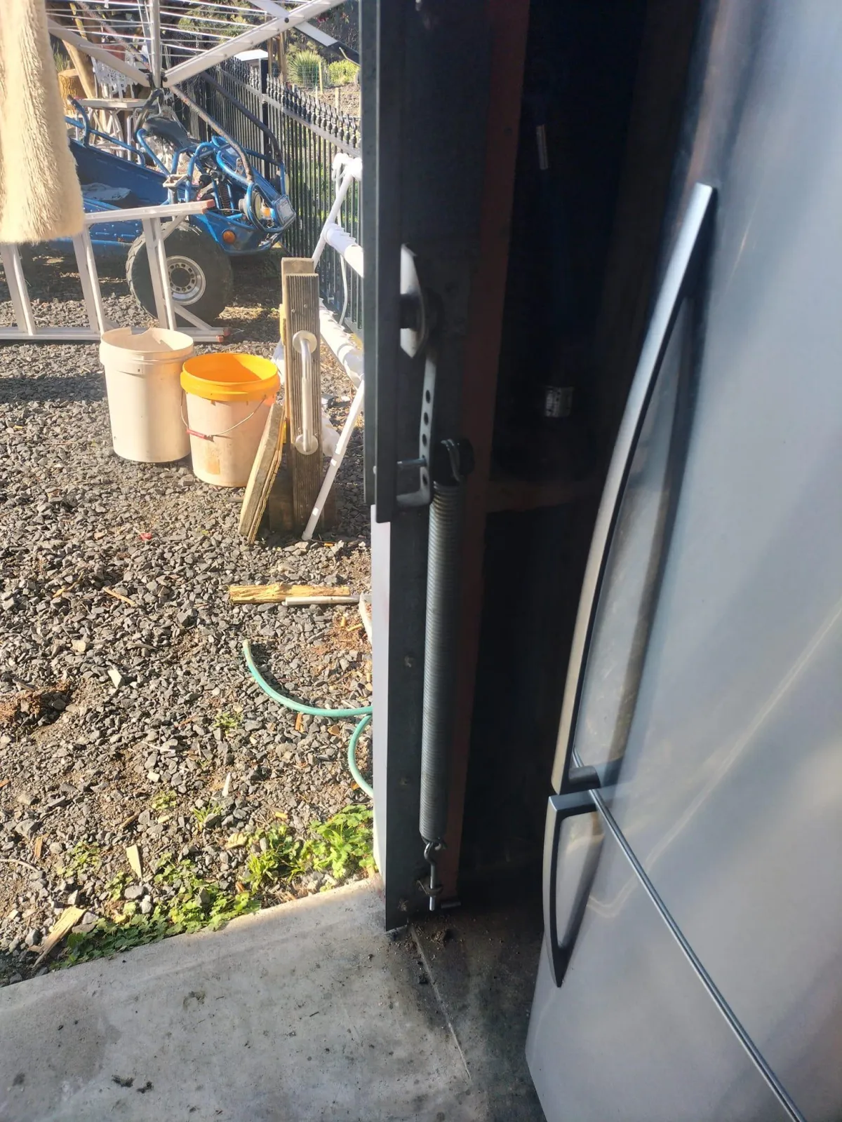 Close-up side view of a garage door torsion spring and track system with garden equipment visible outside.