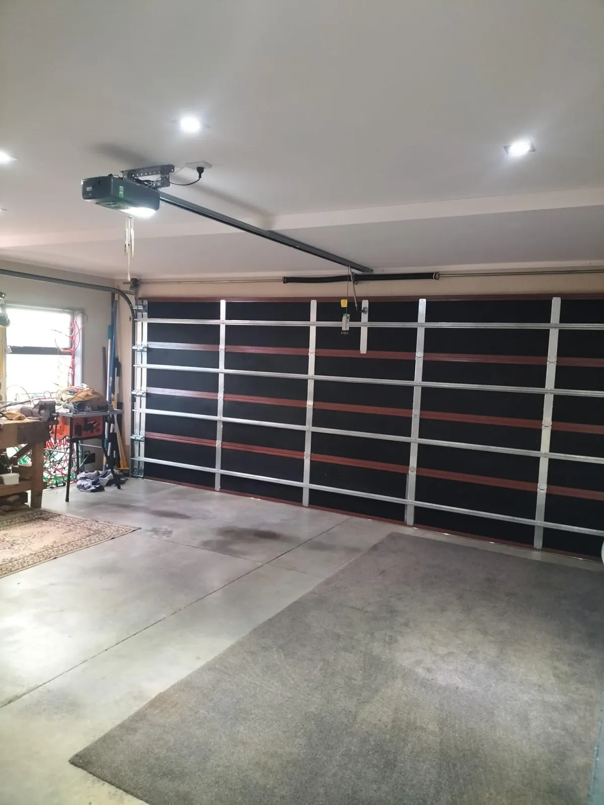 Wide interior view of a garage with a large insulated sectional garage door and ceiling-mounted opener in a clean, well-lit space.