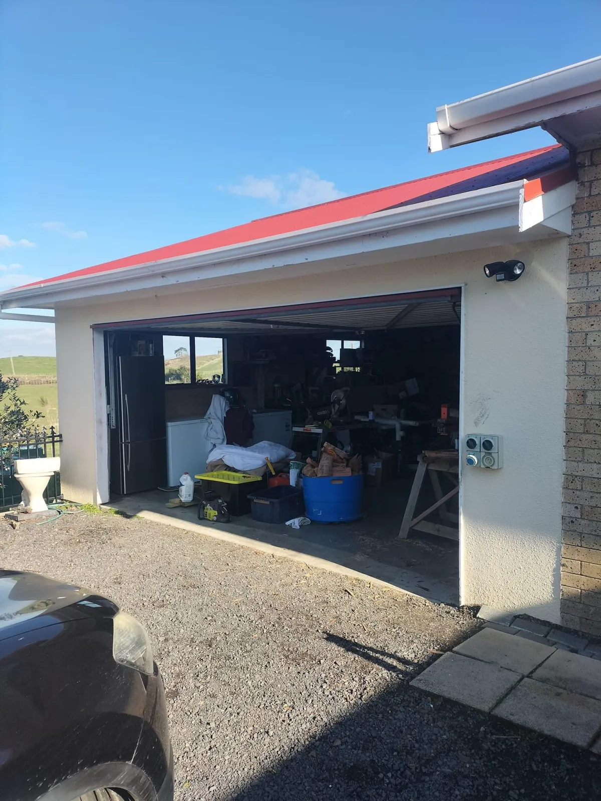 Garage with a partially open custom door, showing tools and storage inside, set against a sunny outdoor backdrop.