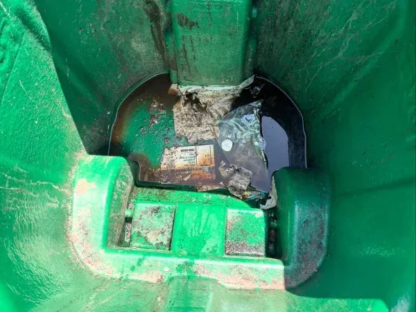 Close-up view of a dirty green trash bin interior with debris and water         Ask ChatGPT