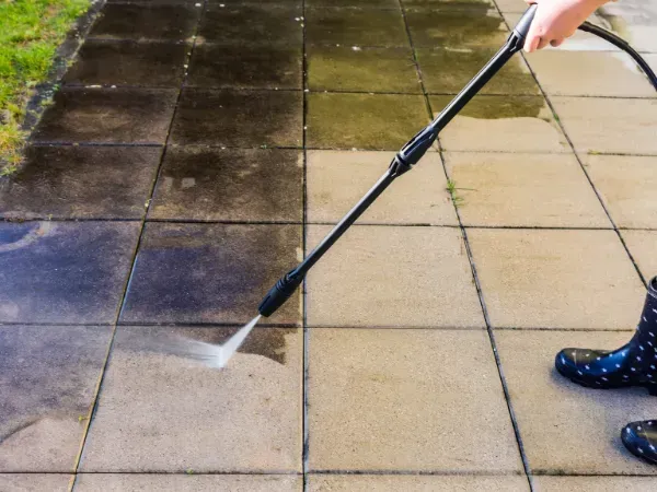 Person pressure washing dirty driveway tiles with visible clean results.