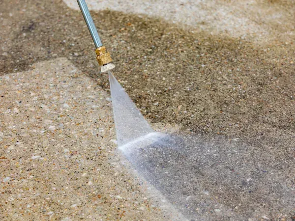 High-pressure water jet cleaning a dirty concrete surface.