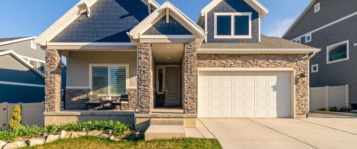 Modern suburban house exterior with stone facade, front porch, and white garage door