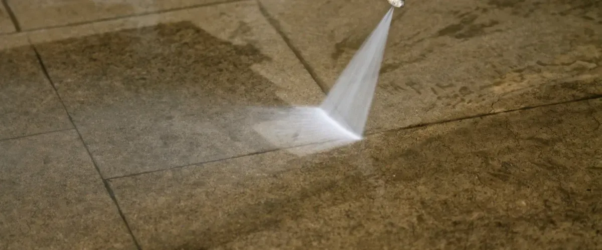 Worker using a high-pressure washer to clean dirt from a stone patio surface.