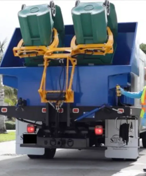 Rear loader garbage truck lifting residential trash bins for collection