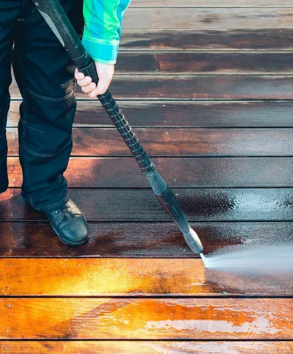 Worker pressure washing wooden deck boards to remove dirt and stains.