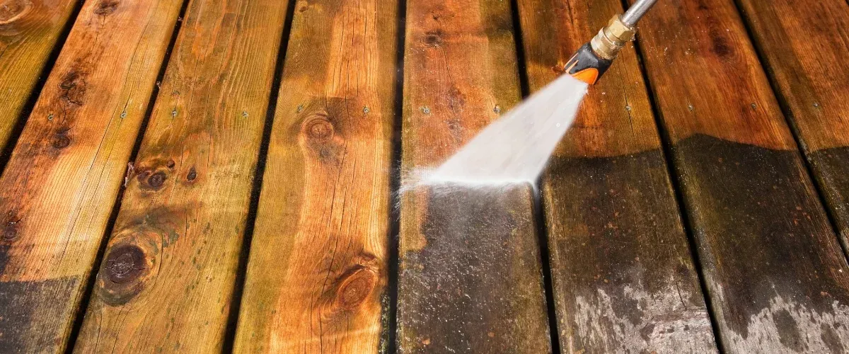 Pressure washing wooden deck boards to remove dirt, mold, and weather stains.