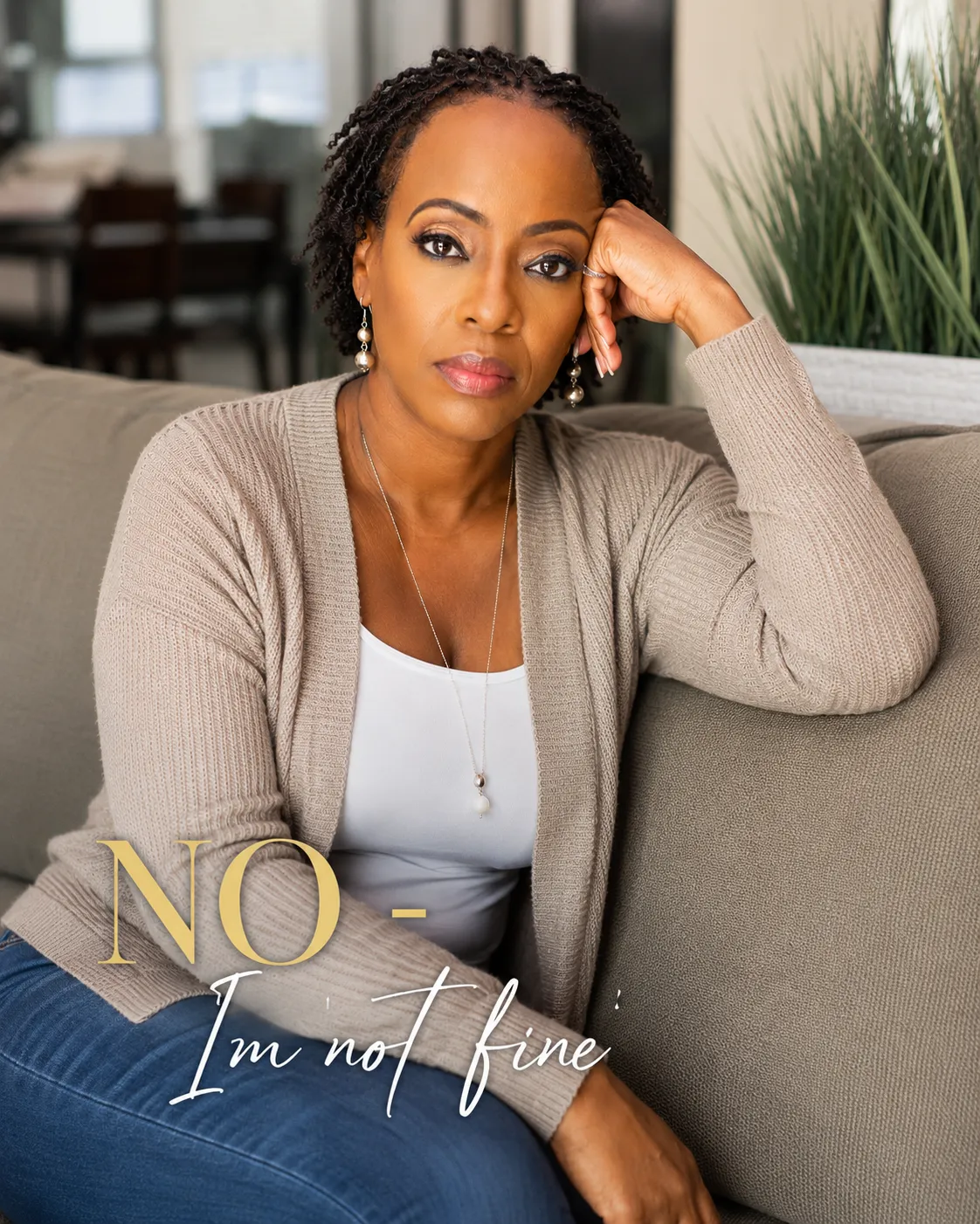 A reflective Black woman sits on a sofa with a serious expression, looking directly ahead. The image features the words, "NO – I'm not fine," representing the hidden emotions many high-functioning women carry behind the words, "I'm fine."