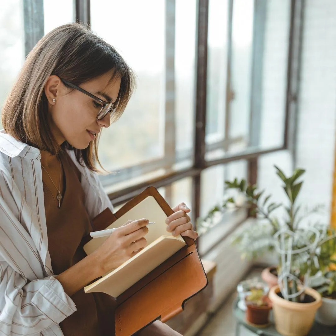 Brunette lady wearing glasses and writing in a journal.